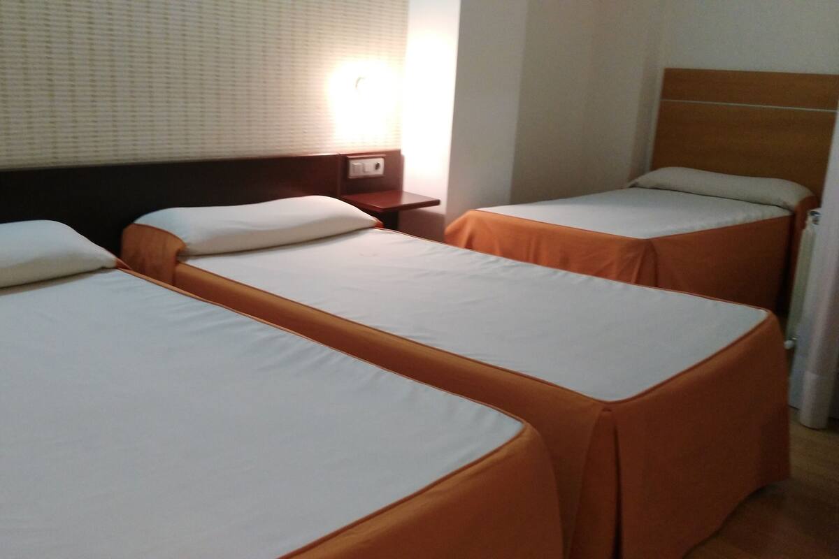 A hotel room with two single beds, a nightstand, and a wall-mounted lamp.