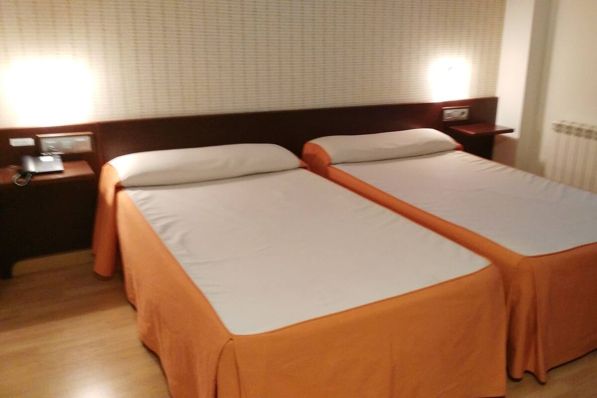 A hotel room with two single beds, a wooden headboard, a bedside table with a lamp, and a telephone.
