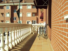 Un balcón con barandilla blanca, un muro de ladrillo y una mesa con sillas.