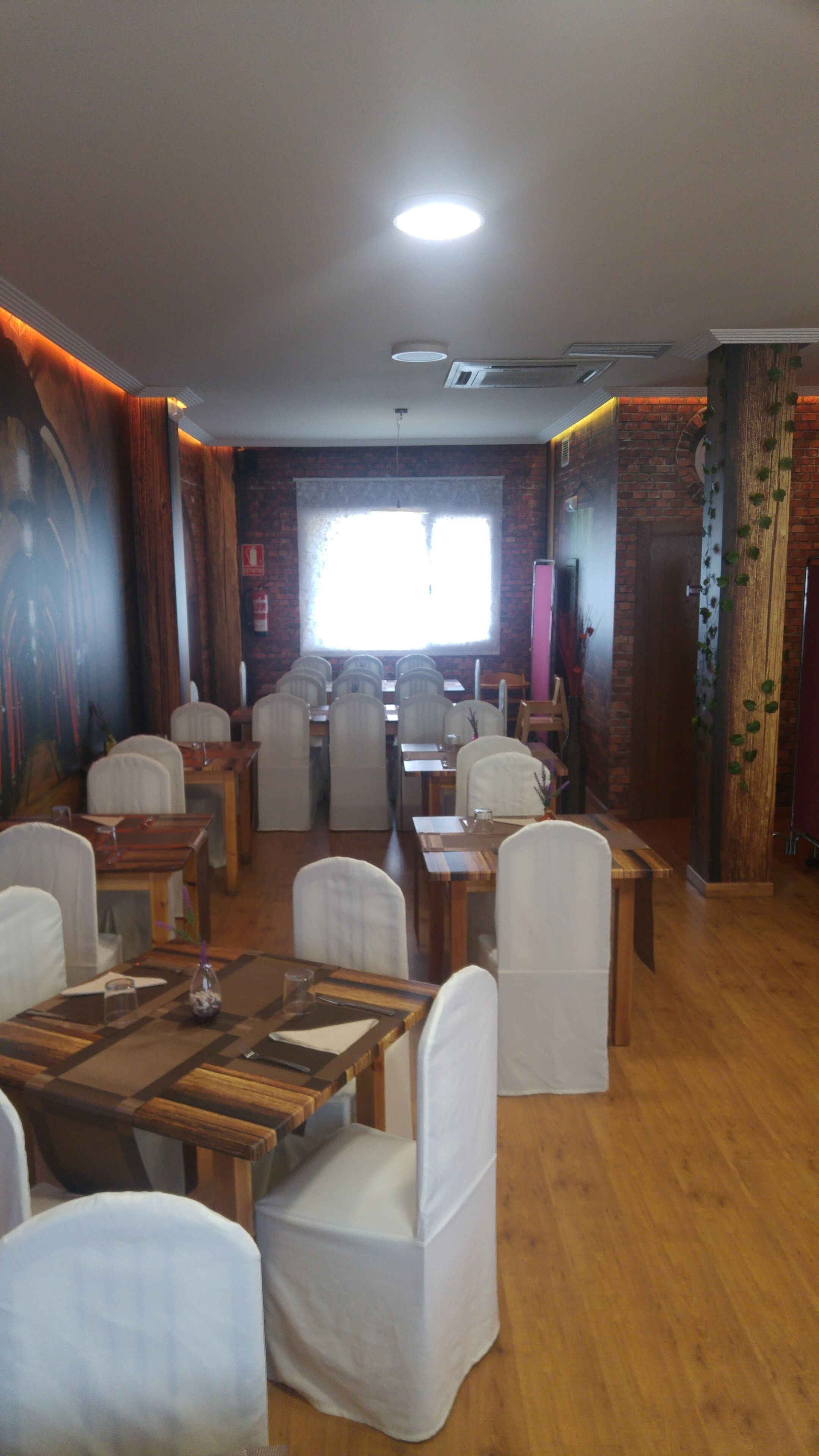 Een restaurant met houten tafels en witte stoelen, bakstenen muren en een groot raam.
