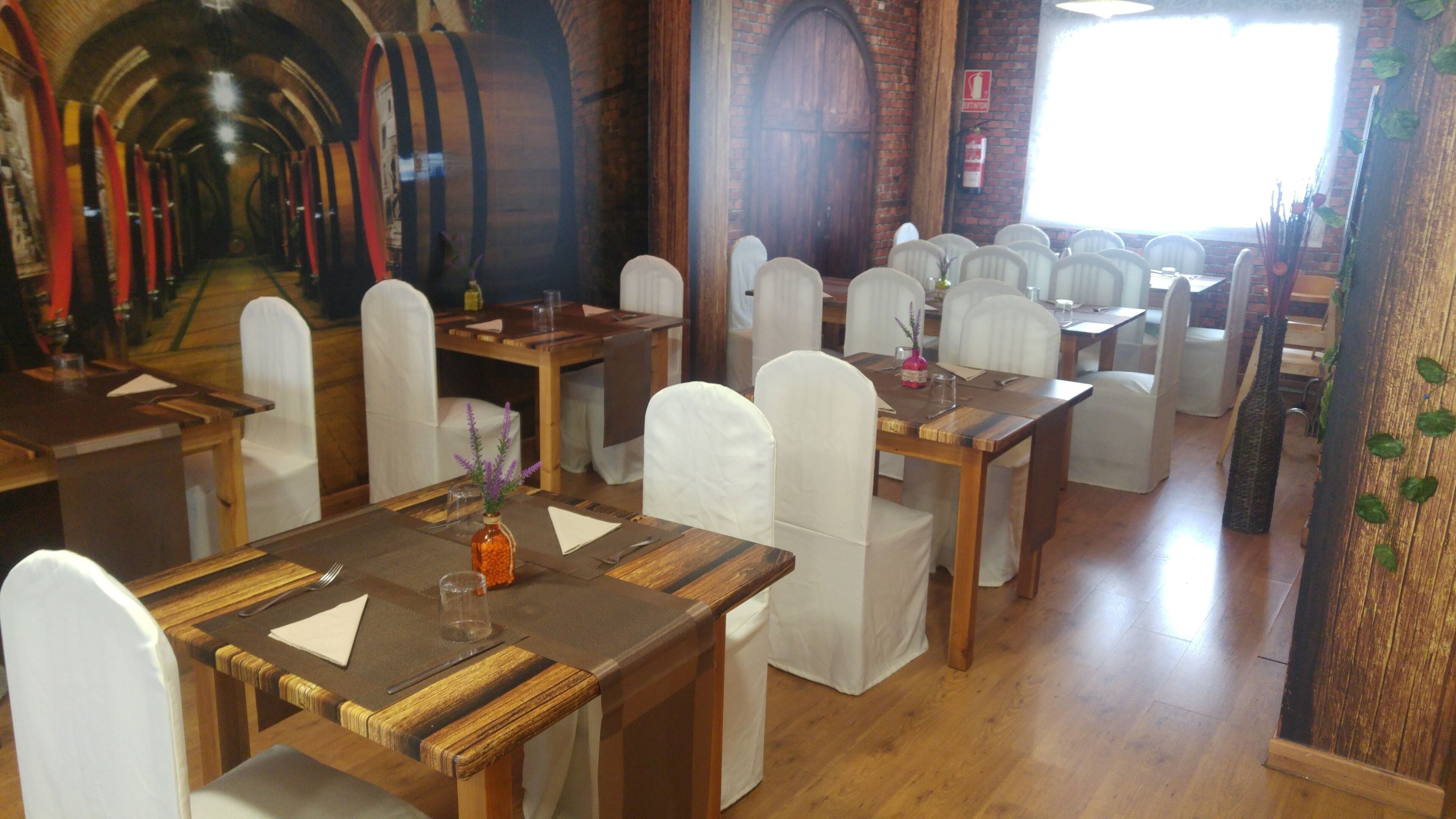A restaurant with wooden tables and white chairs, brick walls, and a large window.