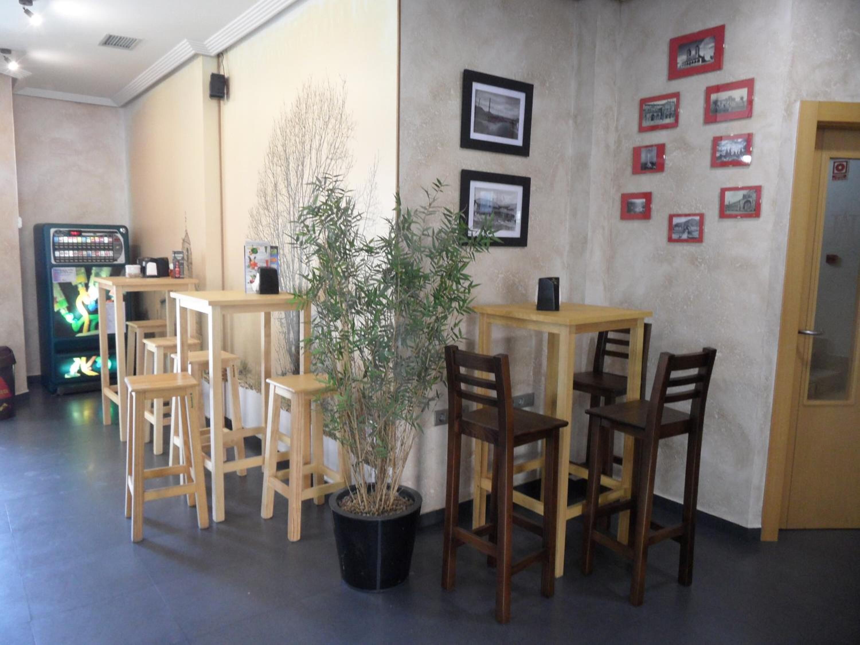 A cafe with wooden tables and chairs, a potted plant, and framed pictures on the wall.