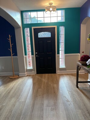 Una habitación con una puerta negra, ventanas amplias y suelo de madera.
