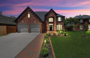 A two-story house with a brick facade, a front yard with a pathway, and a garage.