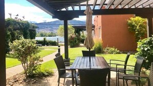Un patio con mesa y sillas, una pérgola y vistas a un jardín ajardinado y montañas.
