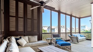 A covered outdoor seating area with a wooden ceiling, large windows, and a view of surrounding buildings. - Carmel Cottage - SOUTH OF 30A, FREE GYM/TENNIS, ELEVATOR, BEAUTIFUL OUTDOOR AREA (Rosemary Beach)
