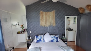 Une chambre avec un grand lit, un ventilateur de plafond, une décoration murale en fibres tressées et une armoire.