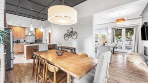 Une cuisine moderne avec des meubles en bois, une table à manger avec des chaises, des luminaires suspendus et une décoration représentant un vélo au mur.