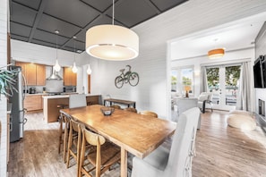 A modern kitchen with wooden cabinets, a dining table with chairs, pendant lights, and a bicycle decoration on the wall.