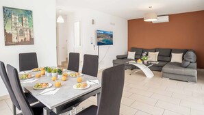 Un salon moderne avec un canapé gris, un coin repas avec une table mise pour le petit-déjeuner, et un tableau représentant une cathédrale accroché au mur.