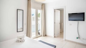 Une chambre d’hôtel avec un lit, un téléviseur fixé au mur, une porte donnant sur un balcon et une fenêtre avec des rideaux.