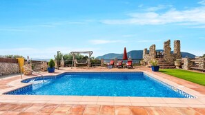 Relax by the clear pool surrounded by terracotta tiles and a pergola, with lounge chairs and a scenic mountain view.