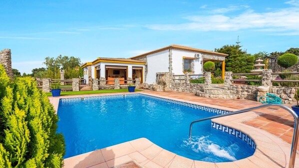 Relax by the serene pool surrounded by lush greenery and a charming stone building.