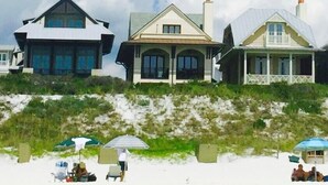 Ein strandnahes Anwesen mit mehreren Häusern, darunter ein großes Haus mit Balkon sowie ein kleineres Haus mit Veranda.