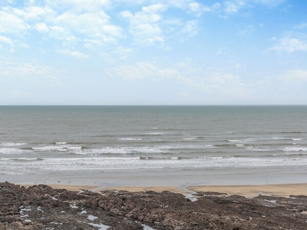 A beach with rocky foreground and calm sea under a partly cloudy sky.