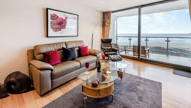 A modern living room with a leather sofa, a glass coffee table, and a large window overlooking the beach. - 2 bedroom accommodation in Westward Ho! (Westward Ho!)