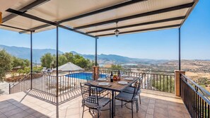 Une terrasse extérieure couverte, dotée d’une piscine, d’une table à manger et de chaises, et offrant une vue sur un paysage montagneux.