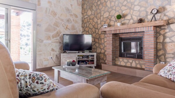 A living room with a stone wall, a fireplace, a television, and a coffee table with decorative items. - El Hoyillo El Gastor by Ruralidays (Cádiz)