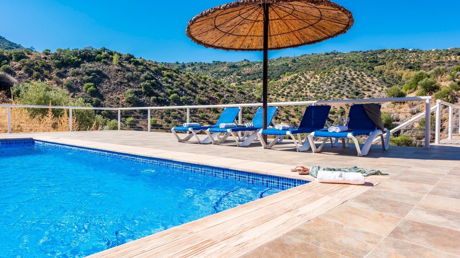 A swimming pool with blue tiles, surrounded by lounge chairs and a large umbrella.
