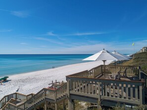 Ein Strand mit einer Holztreppe, die zum Ufer führt, einem weißen Sonnenschirm und einem klaren, blauen Himmel.