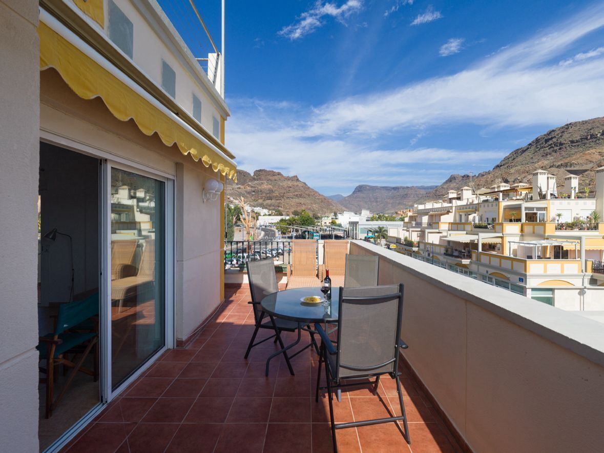 A balcony with a table and chairs, overlooking a residential area with mountains in the background.