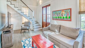 A spacious living room with a staircase, a sofa, a coffee table, and a painting on the wall.