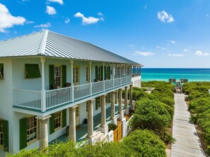 A large, two-story building with a balcony, columns, and a wooden walkway leading to a beach. - Knoepp Cottage - Direct access to beach, Wraparound porch w/Gulf views, (Rosemary Beach)