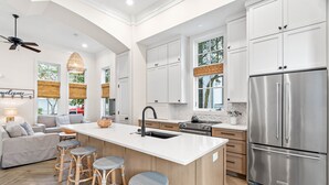 Una cocina moderna con muebles blancos, un refrigerador de acero inoxidable y una isla central con taburetes de bar.