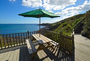 A wooden deck with picnic tables and a green umbrella overlooking a beach. - A fully renovated property, just a short stroll from Coverack’s lovely beach. (Sunny Corner)