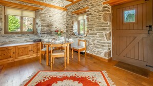 Una habitación rústica de paredes de piedra con una mesa de madera, sillas y un tapete rojo estampado.