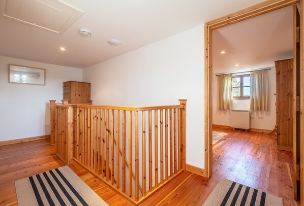 Une pièce au plancher de bois, avec une balustrade en bois, un tableau encadré au mur et une fenêtre avec des rideaux.