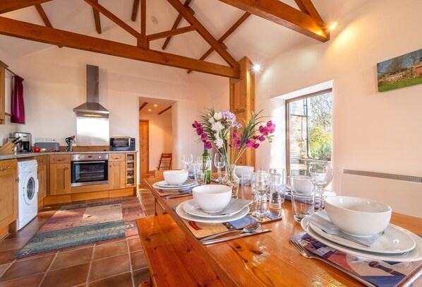 Een moderne keuken met houten balken, een grote eettafel gedekt voor vier personen en uitzicht op het omliggende landschap.