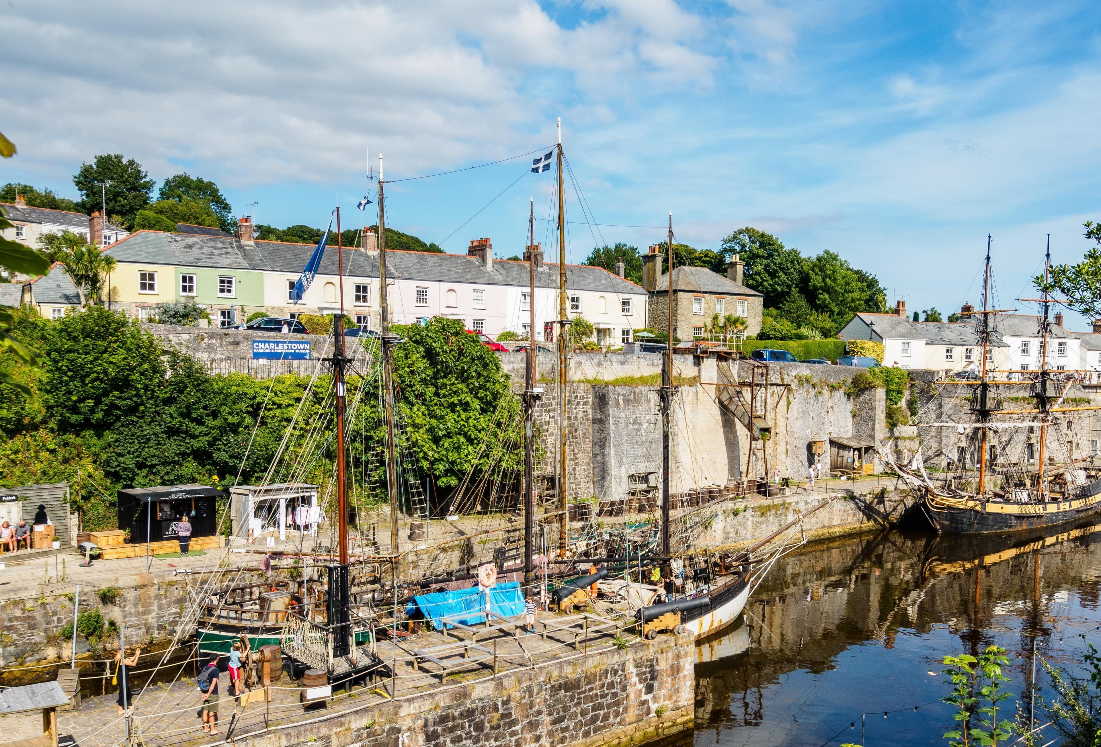 A harbor with a historic ship docked, buildings in the background, and a small dockside café.