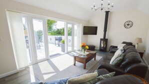 A living room with a sofa, a coffee table with flowers, a fireplace, and a TV mounted on the wall. - A thoughtfully converted three-bedroom barn conversion, near wonderful beaches. (Chacewater)