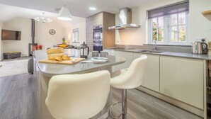 A modern kitchen with a central island, bar stools, a built-in oven, and a window with a view. - A thoughtfully converted three-bedroom barn conversion, near wonderful beaches. (Chacewater)