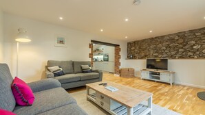 Una sala de estar con un sofá gris, una mesa de centro de madera, un televisor de pantalla plana y una pared de piedra.