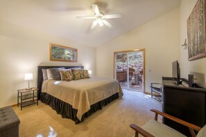 Ein Schlafzimmer mit Bett, Schreibtisch, Stuhl, Deckenventilator und einer Glasschiebetür, die zu einem Außenbereich führt.