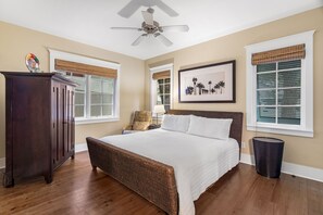 A bedroom with a large bed, a ceiling fan, a dresser, and a framed picture on the wall.