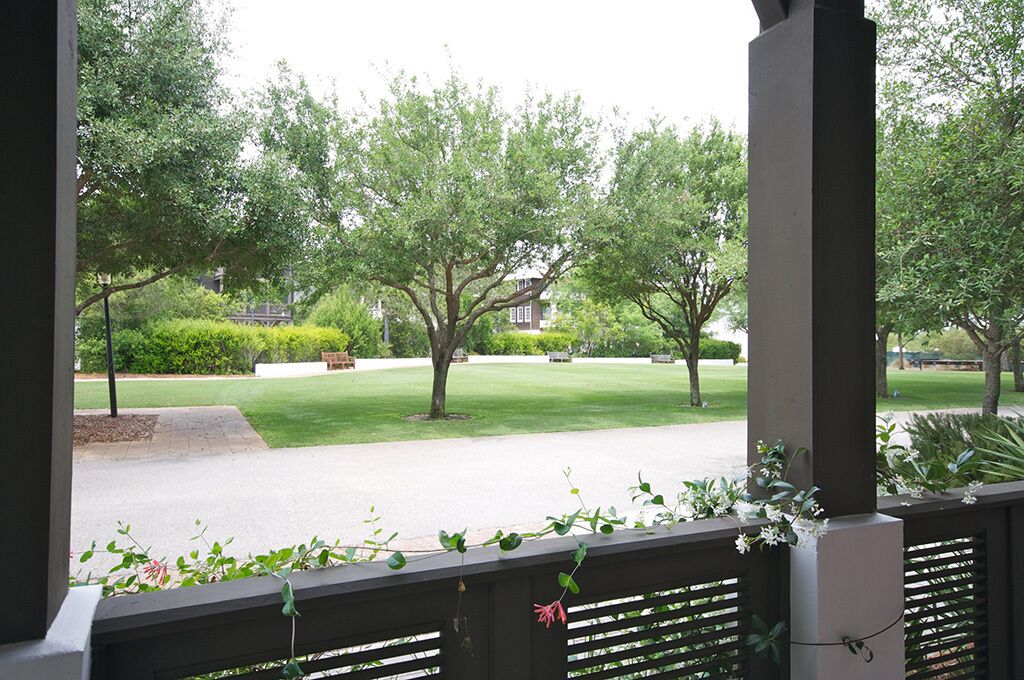 Blick von einer überdachten Veranda mit Rasen und Bäumen im Hintergrund.