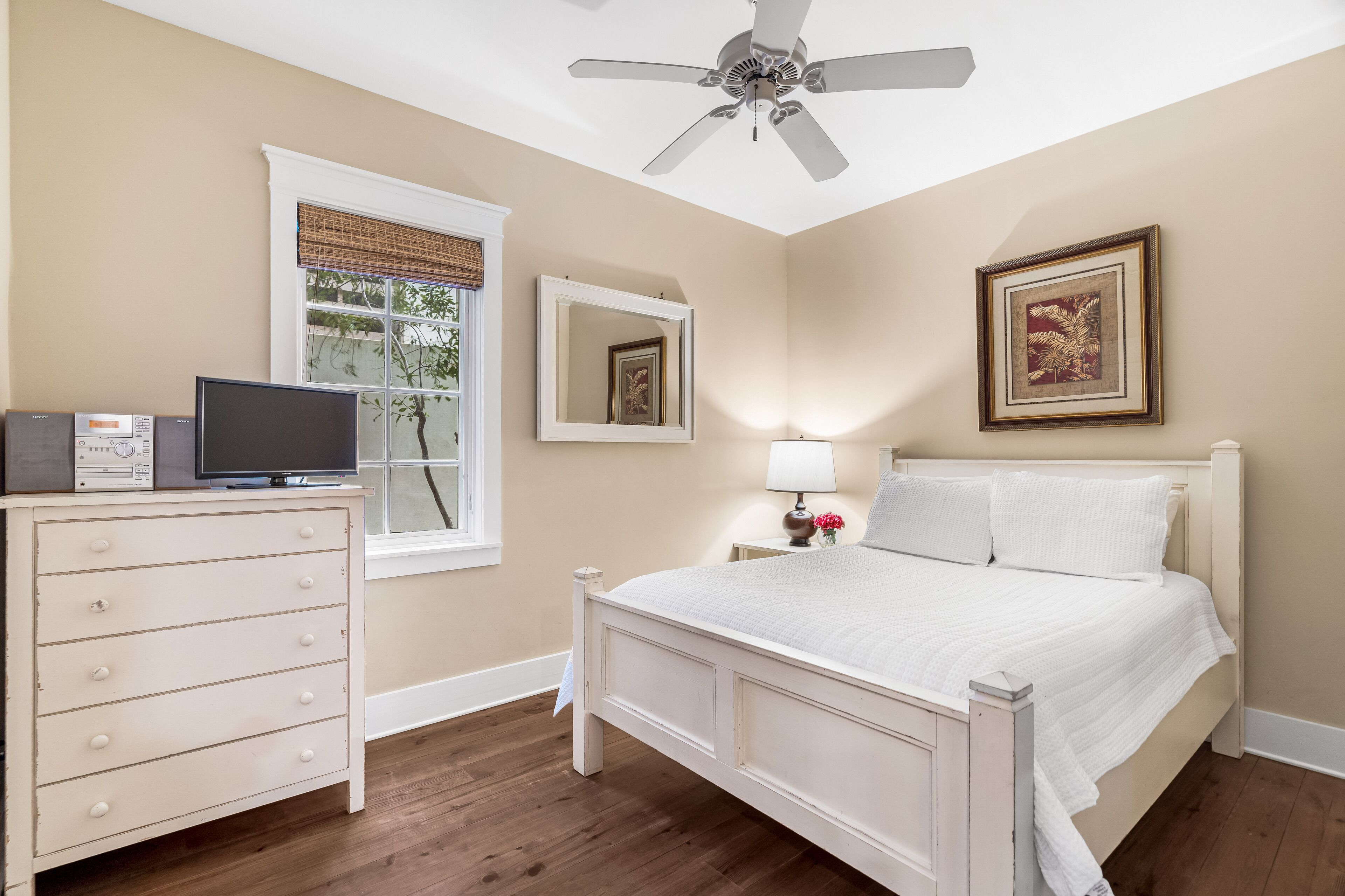 A bedroom with a bed, dresser, television, and framed pictures on the wall.