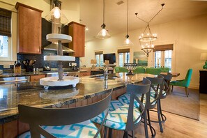 Kitchen features a central island with a multi-tiered sink, modern bar stools, and a dining area.