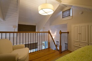 Une pièce avec un escalier en bois, une chaise blanche, un lit recouvert d’une courtepointe à motifs verts et un ventilateur de plafond.