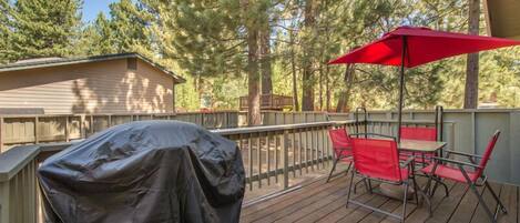 A covered outdoor deck with a barbecue grill, red chairs, and a red umbrella.