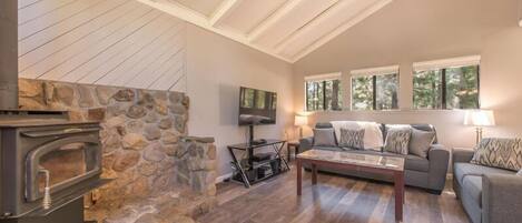 A cozy living room with a stone fireplace, a comfortable sofa, a coffee table, and a TV.