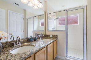 A bathroom with two sinks, a shower, and a large mirror.