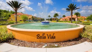 A circular pool with a fountain in the center, surrounded by palm trees and a building labeled "Bella Vida". - Life of Luxury by VillaDirect (Kissimmee)