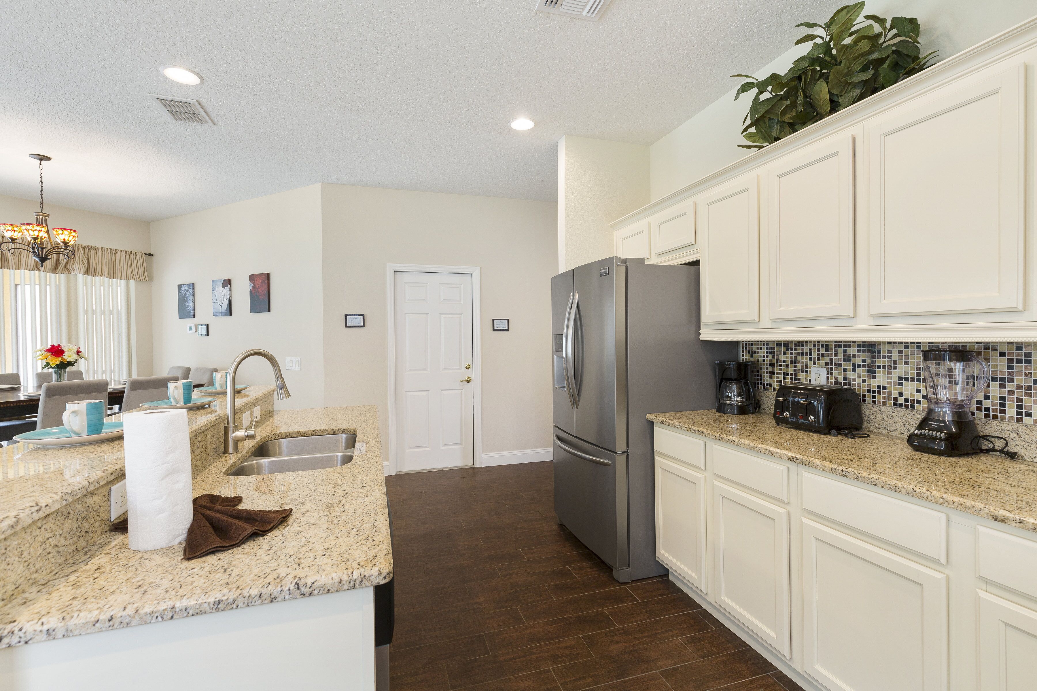 A modern kitchen with white cabinetry, a stainless steel refrigerator, a granite countertop, and a backsplash with a mosaic tile pattern.