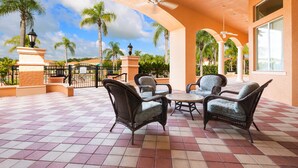 An outdoor patio with wicker furniture, a tiled floor, and a view of palm trees and a pool. - Life of Luxury by VillaDirect (Kissimmee)