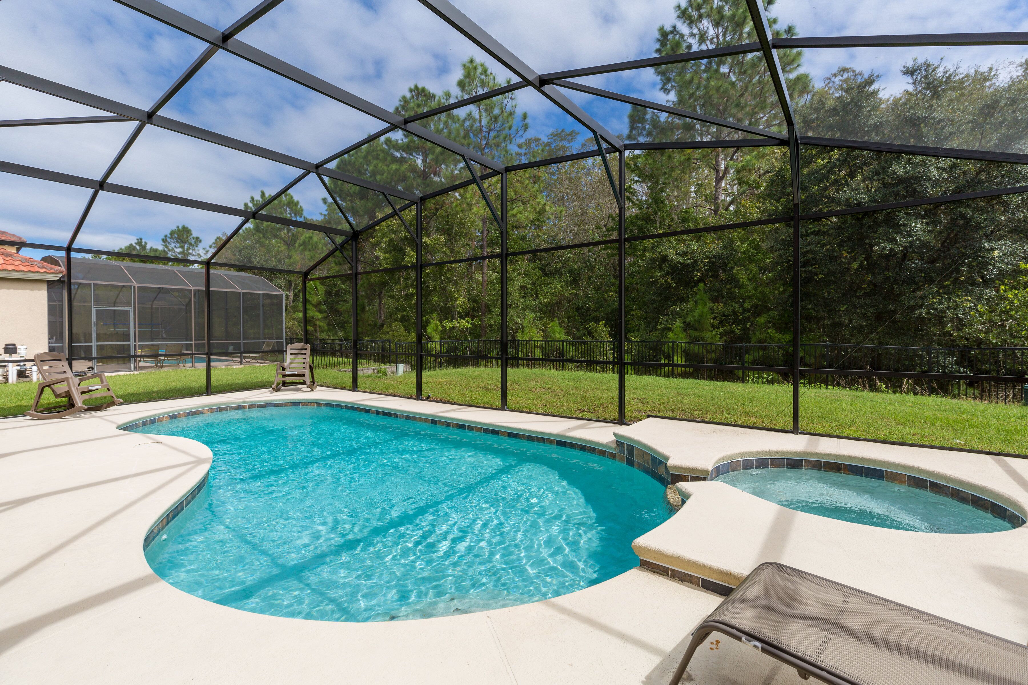 A swimming pool with a glass enclosure, surrounded by a grassy area and trees.