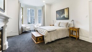 Une chambre à coucher avec un grand lit, une cheminée, une fenêtre avec des rideaux, une chaise et une table de chevet.